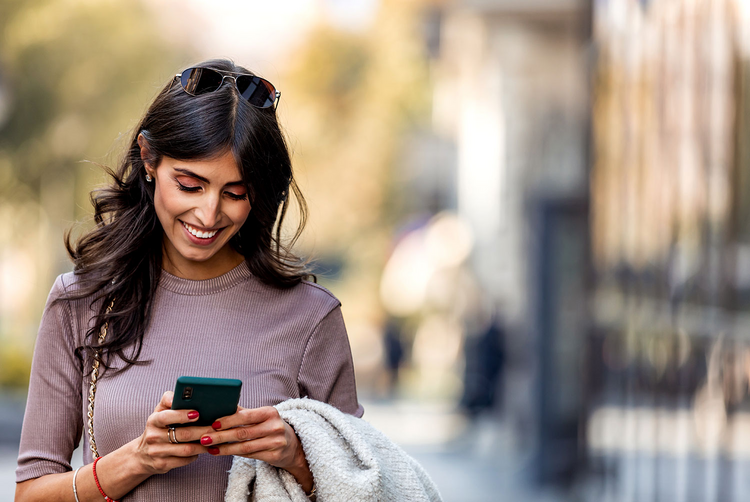 Uma mulher olha para o smartphone que tem na mão com um sorriso